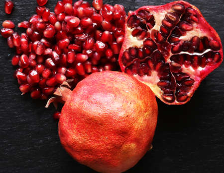 Macro photography of two organic pomegranates one whole and the other cut in half with its seeds on slate background for food illustrationsの写真素材