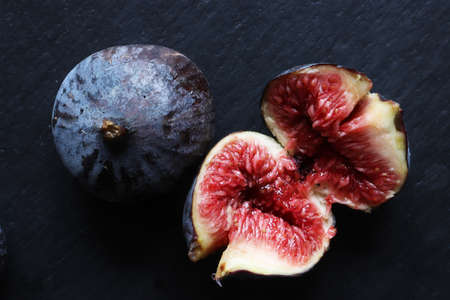 An open fresh red fig and a closed one on slate background for food illustrations