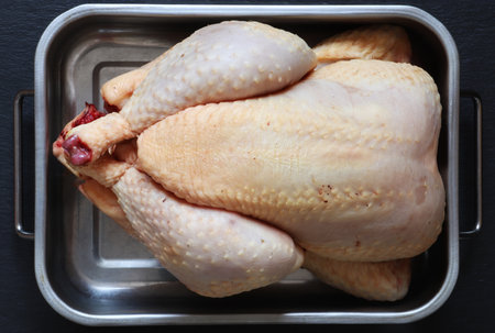 Photography of a raw plucked and prepared chicken in a metal bin on slate background for food illustrationの写真素材