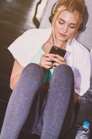 Young woman using smartphone for listening music in the gym