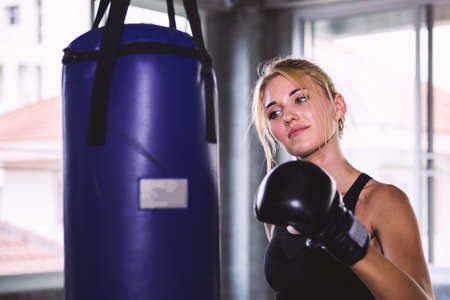 Young female happy to punching a bag with boxing gloveの写真素材