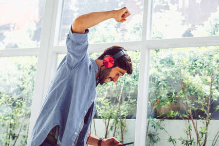 Cheerful male freelancer in headphones standing in home officeの写真素材