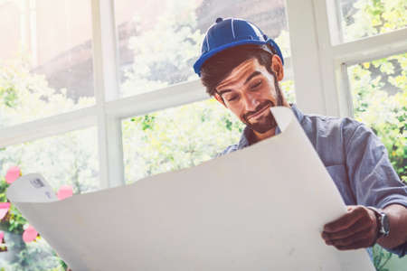 Architect looking at blue print project with a pleasure in the office