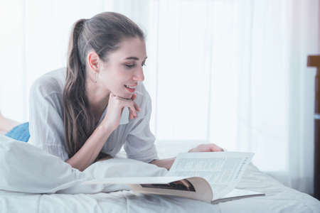 Pretty woman enjoying reading a book while lay down on bed at home.
