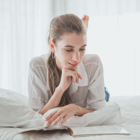 Young woman enjoying reading a book while lay down on the bed.