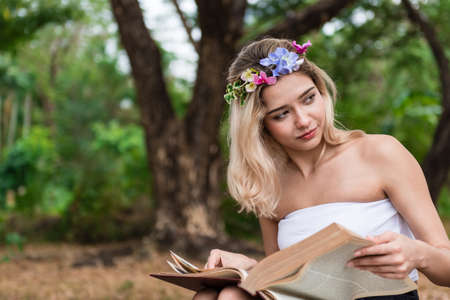 Beautiful woman sitting and reading under the treeの写真素材