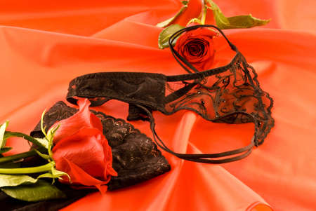 Black strings and stockings with red roses on red backgroundの写真素材