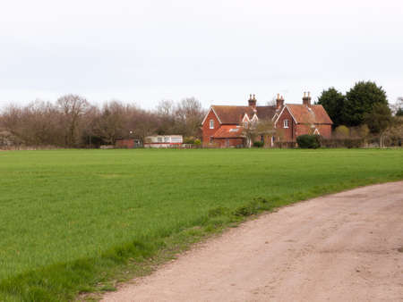 A road through a field of farm with a houseの写真素材