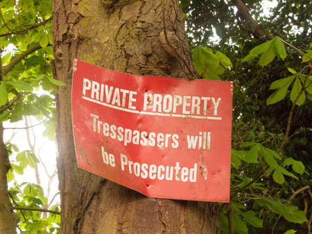A Bent And Dinted Red Sign Attached to A Tree Saying Private Property Tresspassers will be Prosecuted Springの写真素材