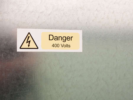 an electric bolt in triangle white yellow and black safety caution sign warning saying danger 400 volts attached to a metal wall background dangerの写真素材