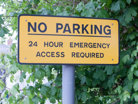 a yellow no parking 24 hour emergency access required post metal sign outside near car par restriction law council england black metal post shrubsの写真素材