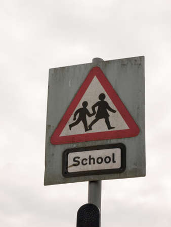 a red white and black school crossing sign with a cloudy sky background danger careful cars motor accidents careful parents and childrenの写真素材