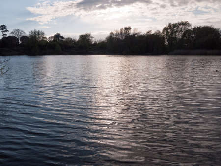 sunset over a lake in spring with moving waves ripples and clouds with trees around water in spring...