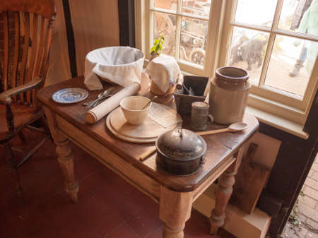 an array of old kitchen utensils and pots and plates and knives and forks on a nice wooden table near a window on a sunny dayの写真素材
