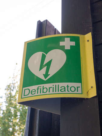 a sign outside indicating a nearby defibrillator yellow and green medical help for heart strokeの写真素材
