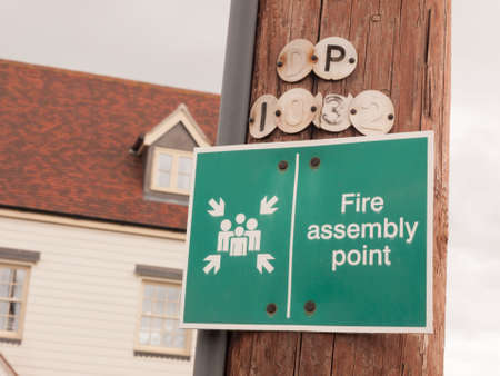 a green sign outside on a wooden pole saying fire assembly point fire warningの写真素材