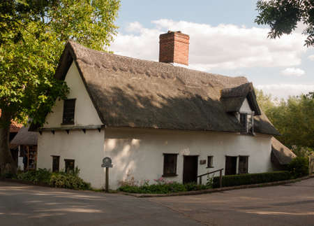 an old white barn cottage with thatched roof in summer light; UKのeditorial素材