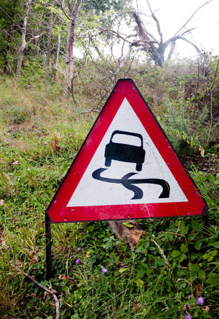 a red triangle driving sign on the side of road on grass; UKのeditorial素材