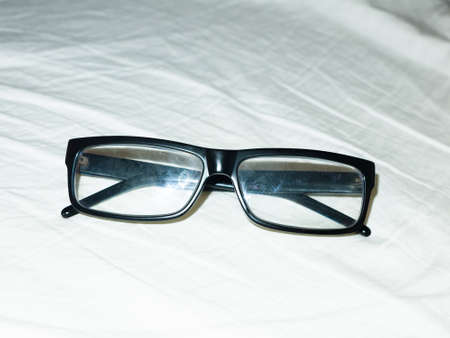 folded up black glasses resting on white bed sheet.の写真素材