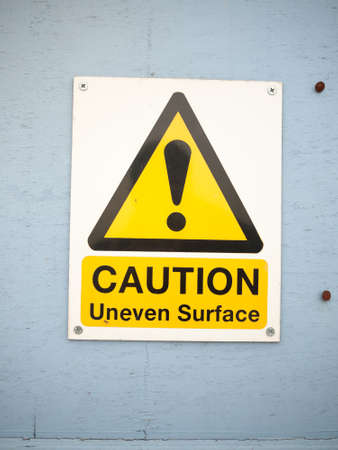 a close up caution uneven surface sign on blue wall seafront; England; UKの写真素材
