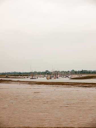lots of moored boats in the river in the distance behind mud overcast day sky empty; England; UKの写真素材