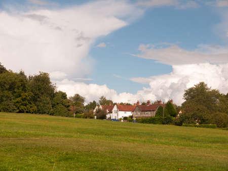 interesting sloped green lawn with country houses in background and blue and white cloud sky; England; UKの写真素材