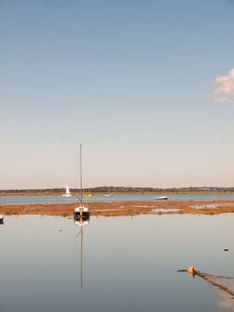 boat moored in estuary scene with mast reflected in water blue sky; essex; england; UKの写真素材