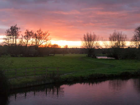 red sun setting sky dramatic autumn over empty open green countryside night dark lake; essex;...