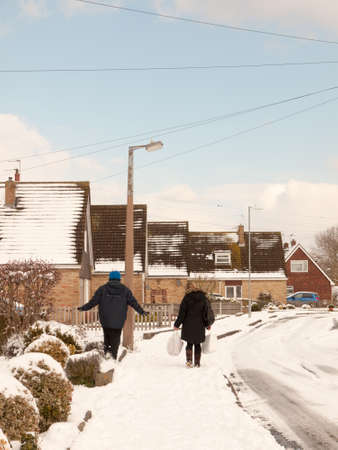 mother and son walking down street with snow in winter uk estate from behind; essex; england; ukの写真素材