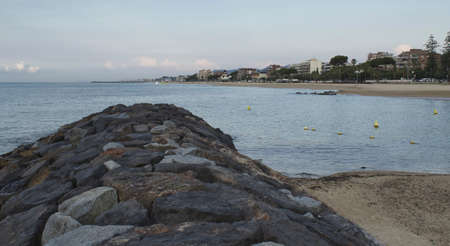 closeup of stone breakwater with seaside village and sky backgroundの写真素材