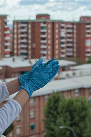gloved hands clapping from a balcony with the city in the background
