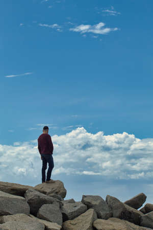 standing man on top of a stone breakwater looking at the horizon with clouds in the backgroundの写真素材