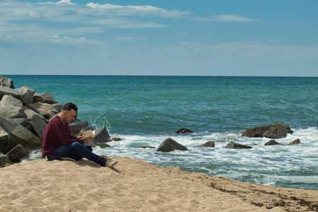 man sitting on the sand reading a book on the seashoreの写真素材