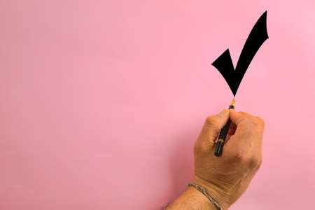 hand holding a pen writing an OK sign on a pink backgroundの写真素材