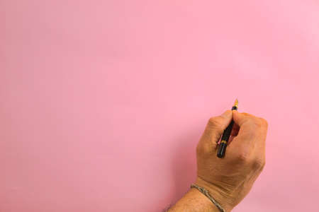 hand holding a pen about to write on a pink backgroundの写真素材