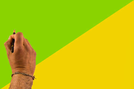 hand holding a pen about to write on green and yellow background