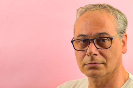 close-up gray haired man looking straight ahead on a pink background