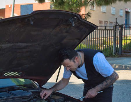 mature man repair a breakdown in his car engine with tools on the side of the road