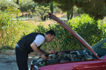 mature man fixing a breakdown in his car engine with tools on the side of the roadの写真素材