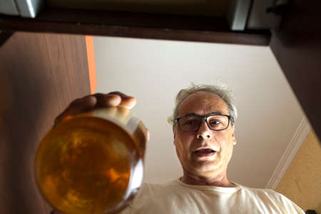 mature man with gray hair picking up a bottle from the bar cabinet at homeの写真素材