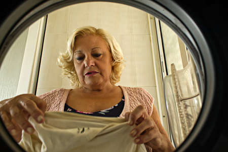 mature woman taking clothes out of the washing machine seen from insideの写真素材
