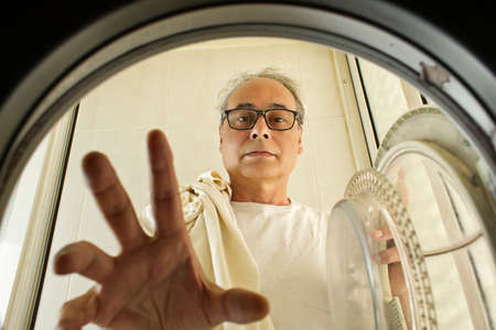 mature man taking clothes out of the washing machine seen from insideの写真素材