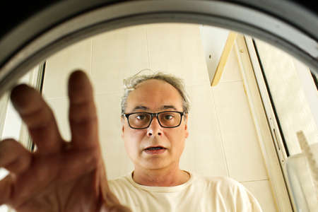 mature man taking clothes out of the washing machine seen from insideの写真素材