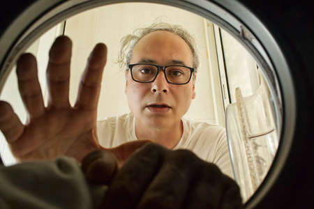 mature man taking clothes out of the washing machine seen from insideの写真素材