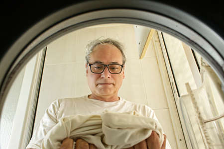 mature man taking clothes out of the washing machine seen from insideの写真素材