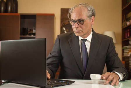businessman having coffee and teleworking from home with laptop due to restrictionsの写真素材