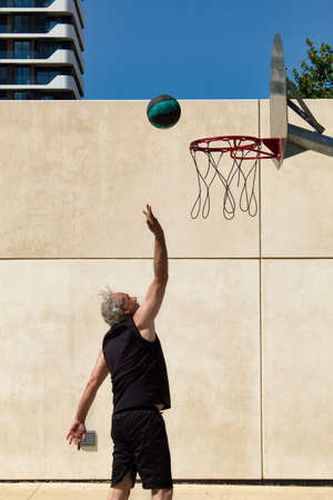 mature man playing basketball alone on a street court with metal basket