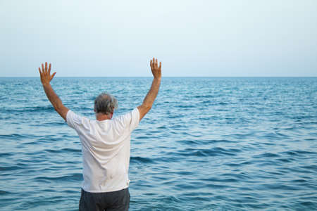 view from behind of mature man with gray hair enjoying on seashoreの写真素材