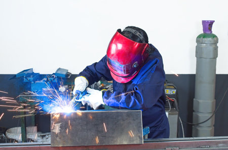 woman with gloves working in a workshop welding metal with protection mask and overallsの写真素材
