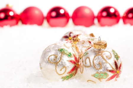 White glass baubles and a line of red baubles in the background on snowの写真素材